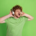 Joven escuchando música a alto volumen en auriculares, una de las principales causas de pérdida auditiva temprana